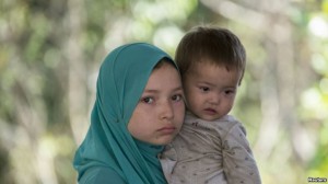 FILE - A suspected Uighur from China's troubled far-western region of Xinjiang, holds an infant as they rest inside a temporary shelter on March 14. They were detained at the immigration regional headquarters near Thailand-Malaysia border.